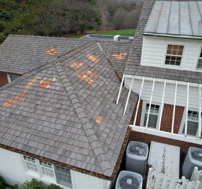 A Roof With Grey Shingles That Has Been Patched Up With Wood Colored Shingles