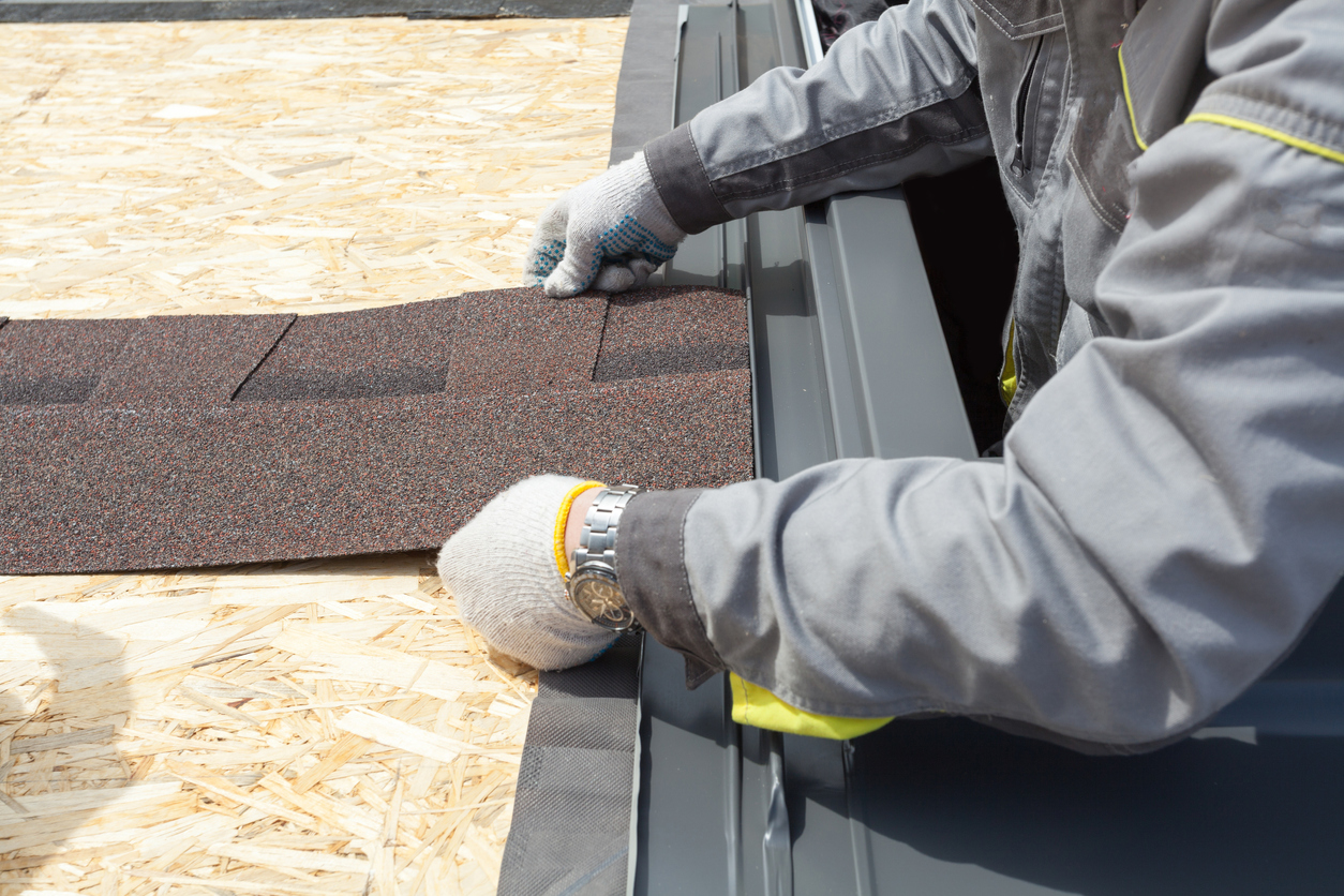 A roofer carefully places shingles down on a roof.